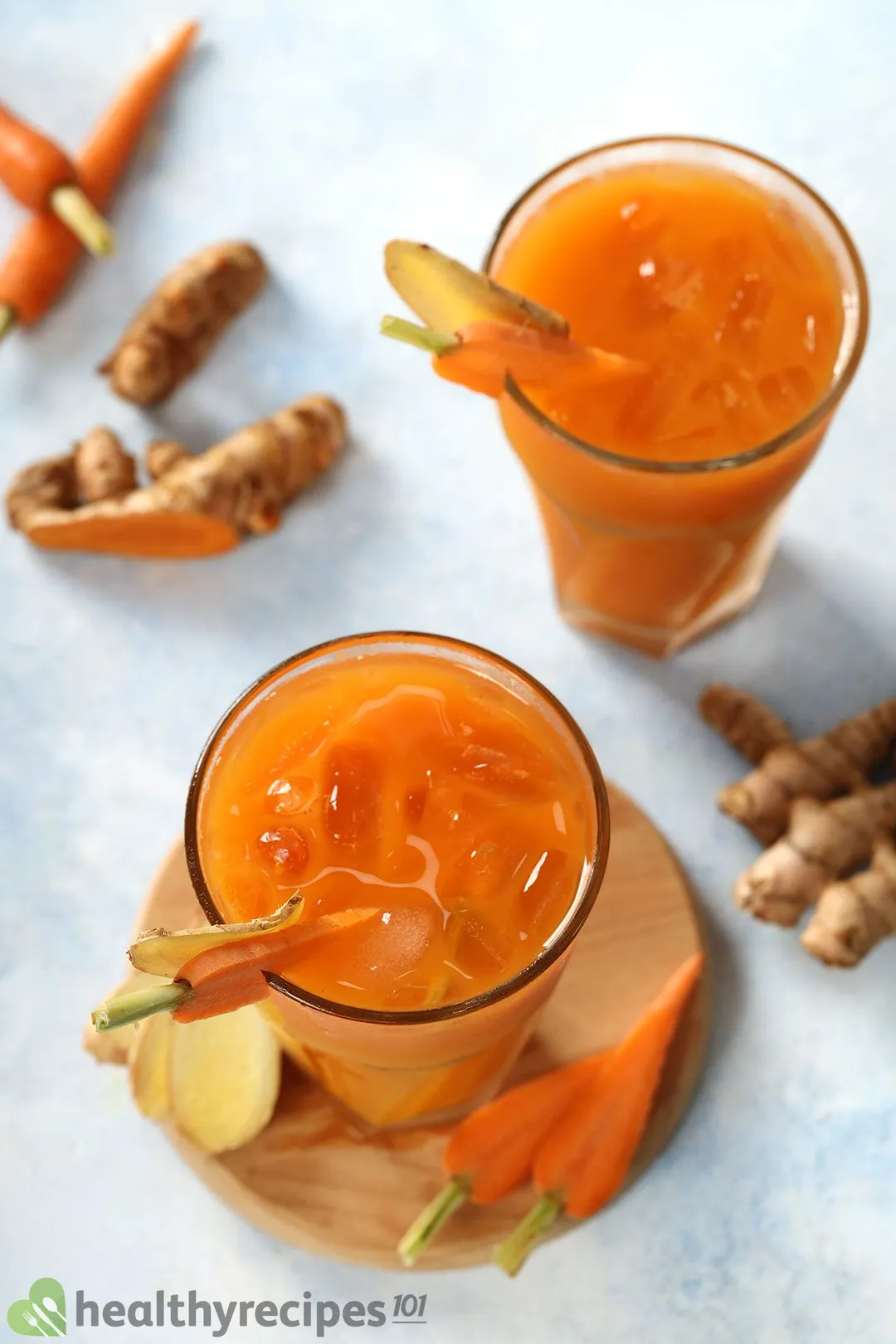 A high-angle shot of two Carrot Ginger Turmeric Juice glasses placed near baby carrots and ginger.
