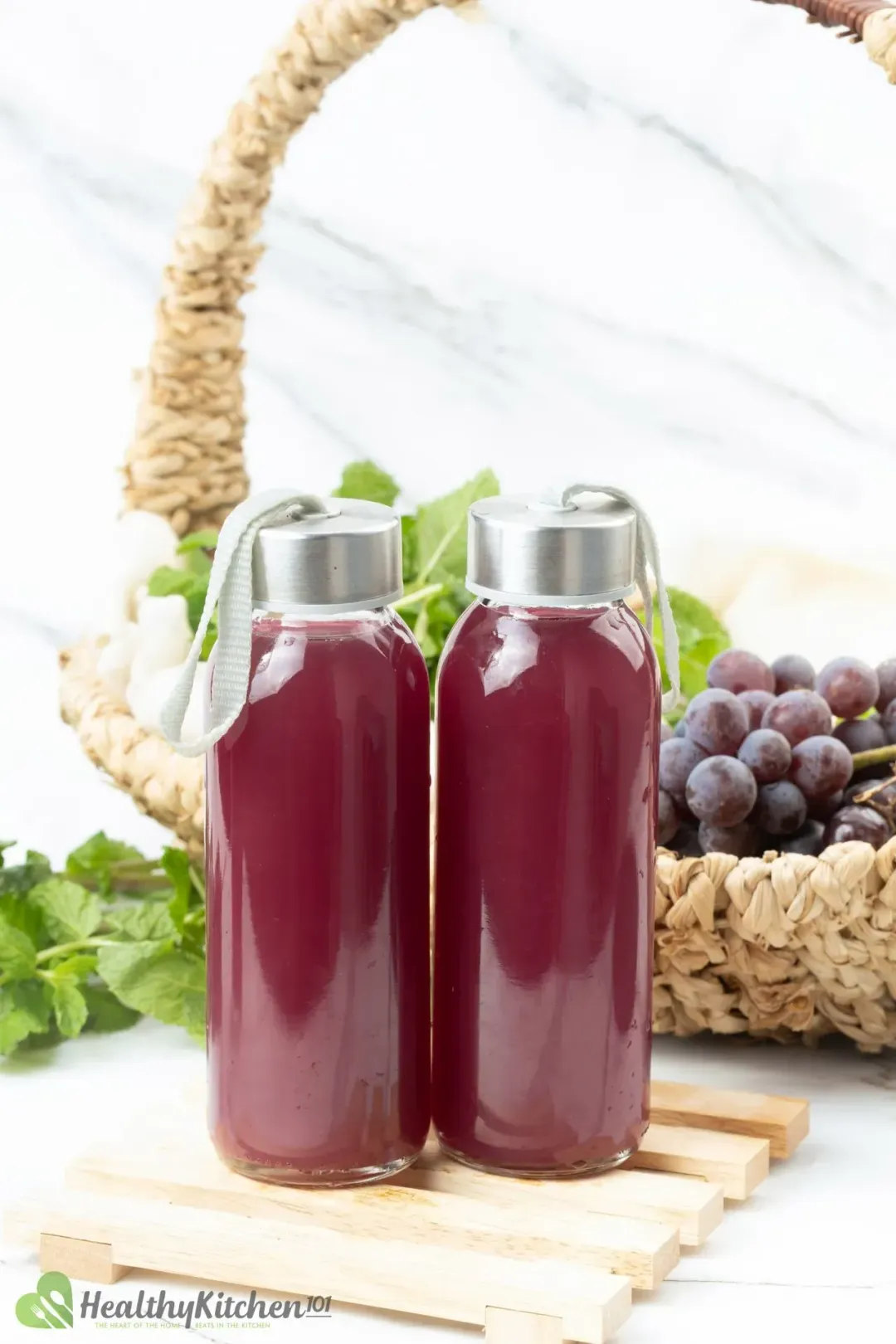 Two bottles filled with red grape juice and cider drink, next to a basket of grapes