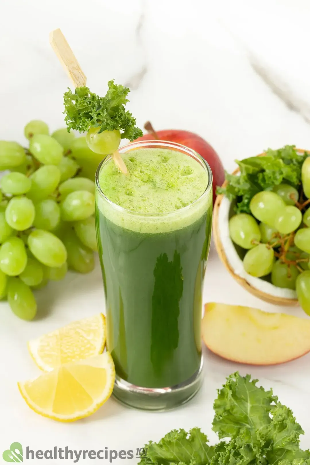 A picture of a glass of green machine juice surrounded by some lemon wedges, grapes, and kale that are taken from above