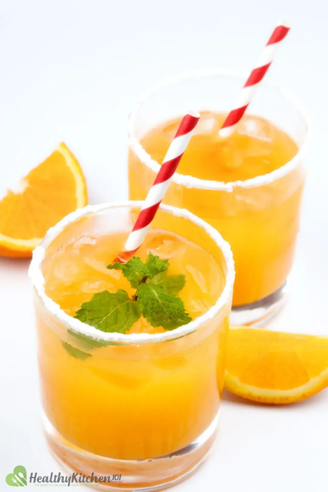 Two whiskey and orange juice cocktails in two short iced glasses with mints and red-striped straws