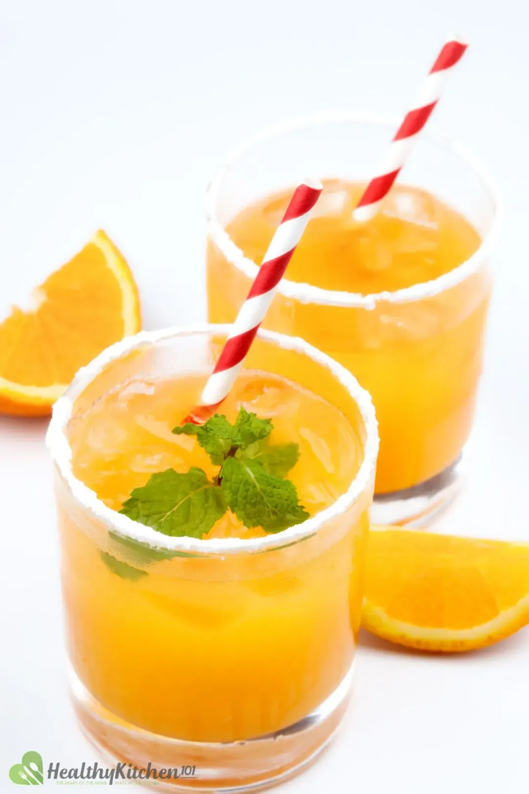 Two whiskey and orange juice cocktails in two short iced glasses with mints and red-striped straws