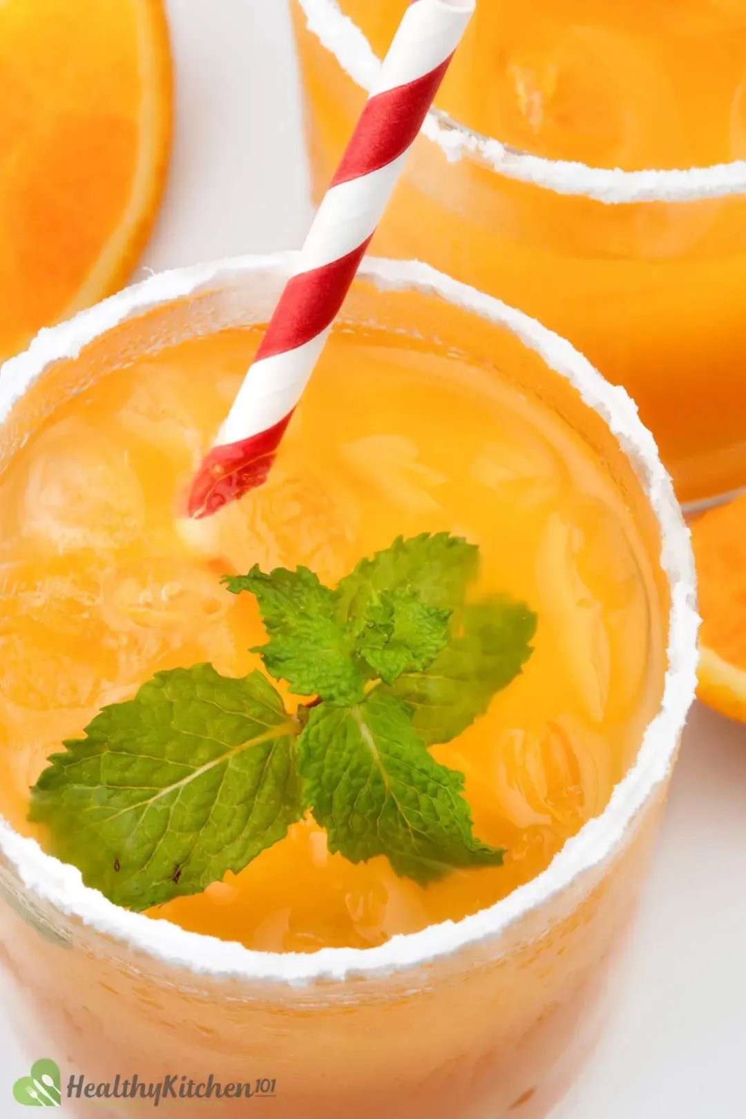 A close-up shot of a whiskey and orange juice cocktail glass with mints, straw, and powdered sugar on the rim