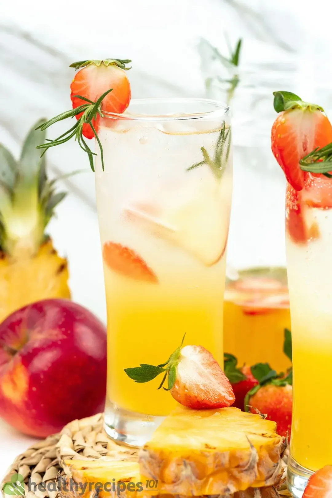 A tall glass of orange jungle juice cocktail, next to some fruits and another glass