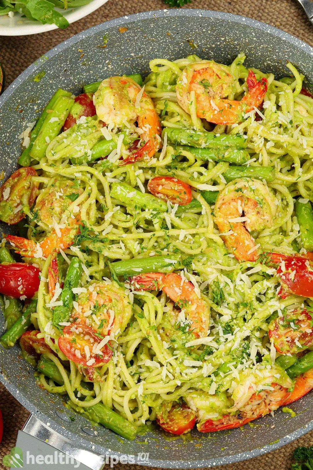 A large pan filled with avocado pasta, cooked shrimp, and some cherry tomatoes.