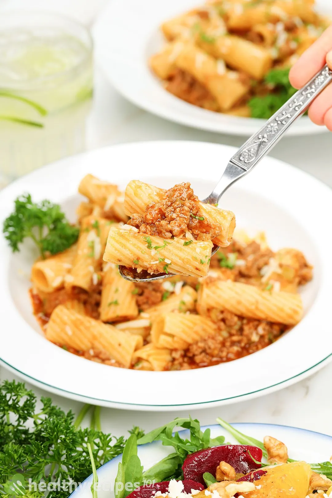 A hand using a fork to scoop up some Pasta Bolognese from a plate.