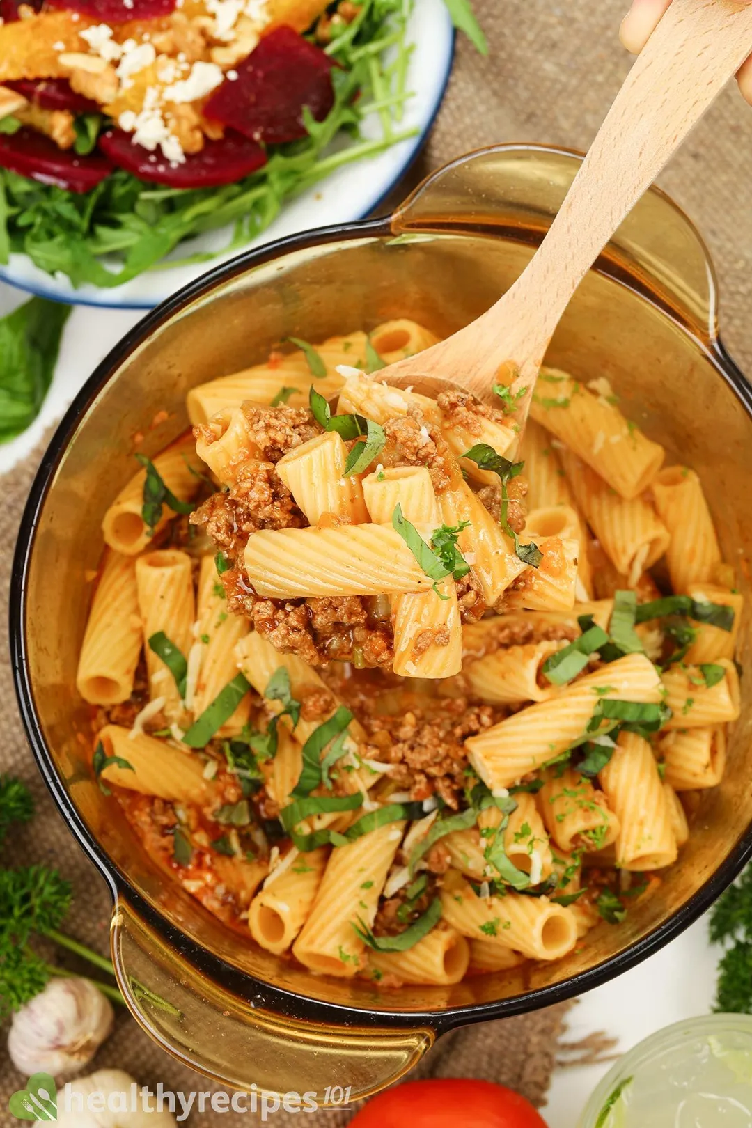 A wooden ladle scooping pasta from a glass saucepan filled with Pasta Bolognese.