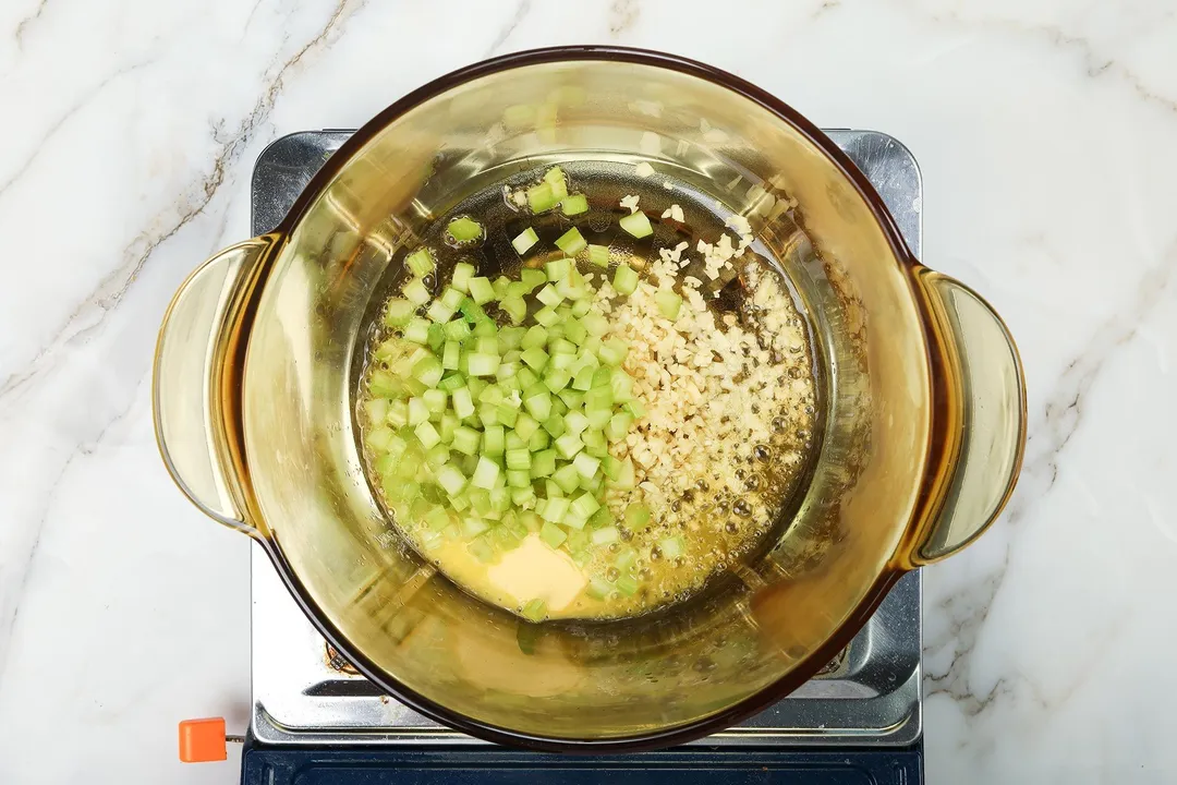 A saucepan cooking chopped celery and diced onion on a portable gas stove.