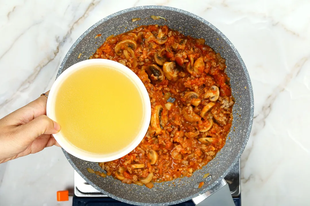 a bowl of chicken broth on top of a skillet of mushroom sauce