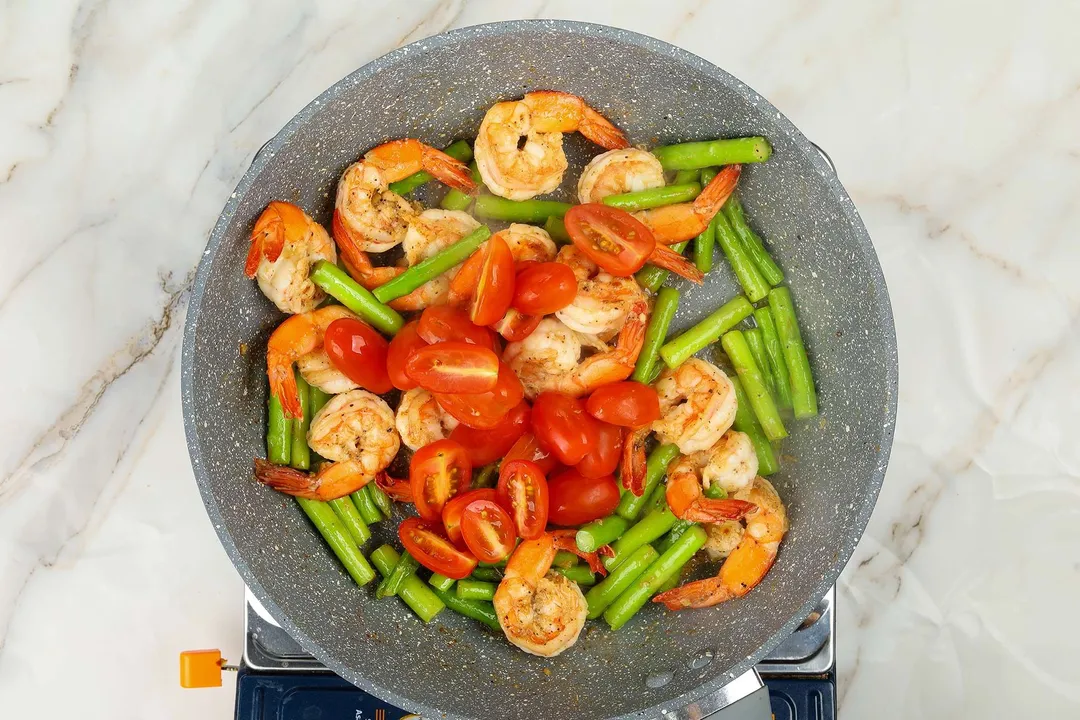 A pan cooking shrimp, asparagus, and tomatoes.