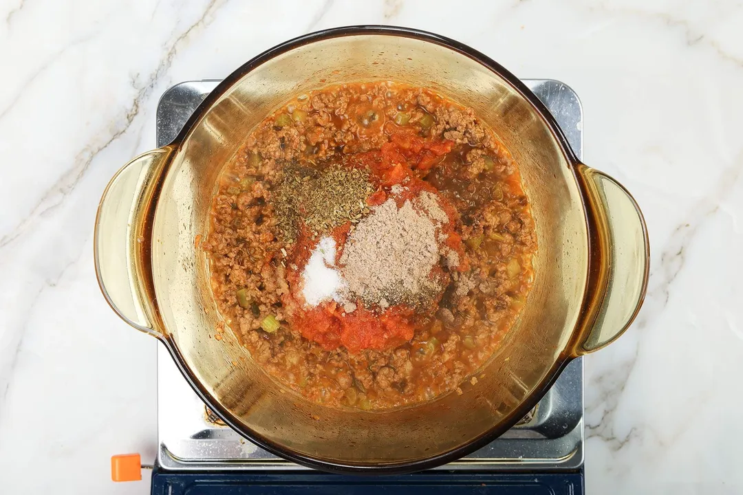 A saucepan cooking ground beef with piles of spices in the center.