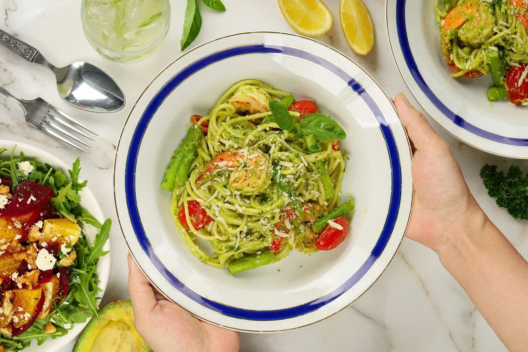 Two hands holding up a plate of avocado pasta.