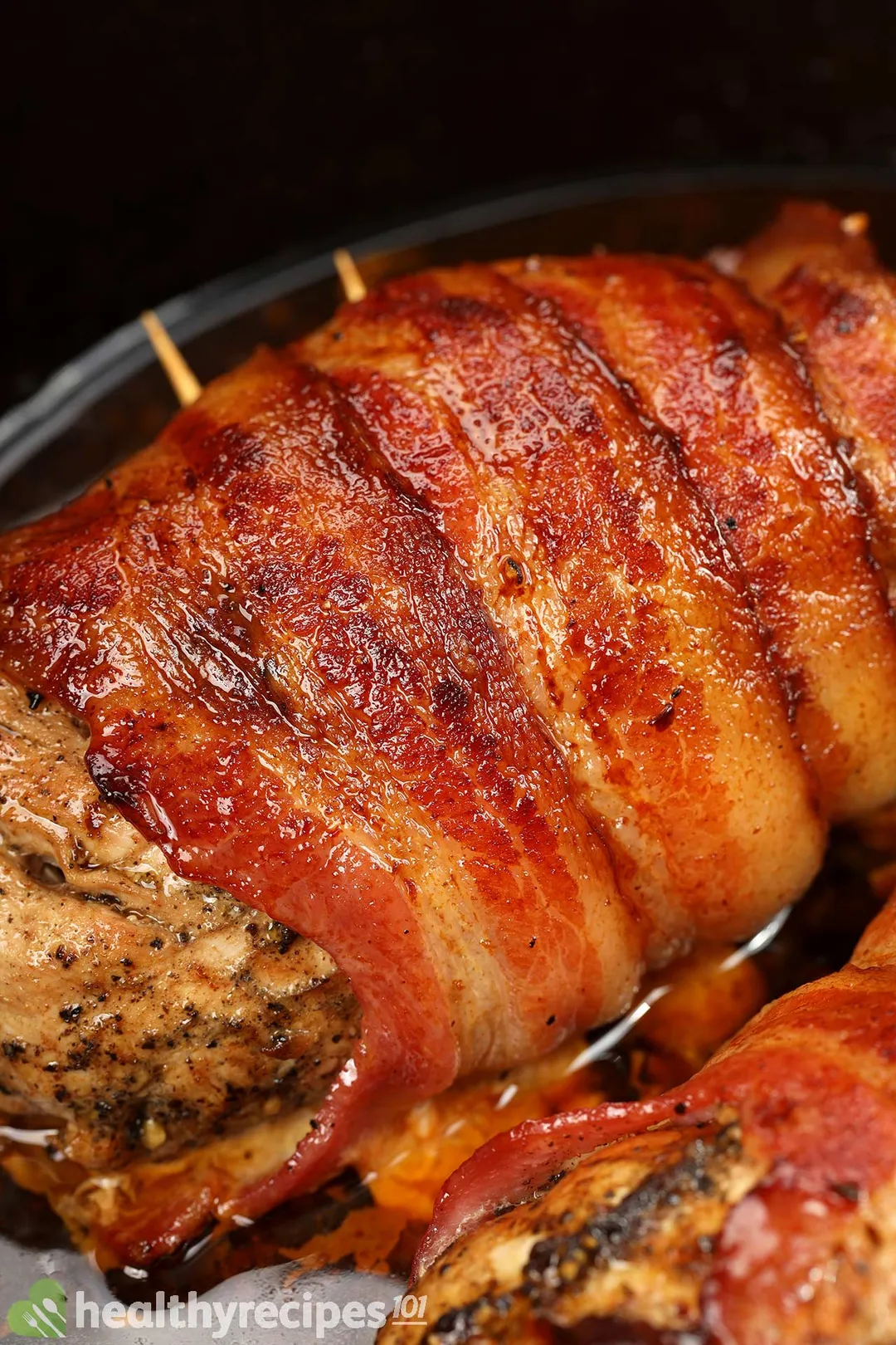 a close shot of cooked bacon wrapped pork tenderloin in a cast iron skillet