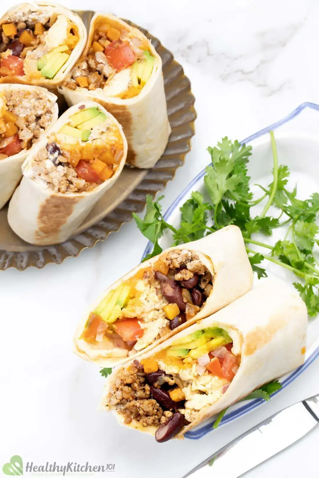 Cut-up rolls of burrito, filled with beans, ground meat, and colorful vegetables on plates with cilantro sprigs