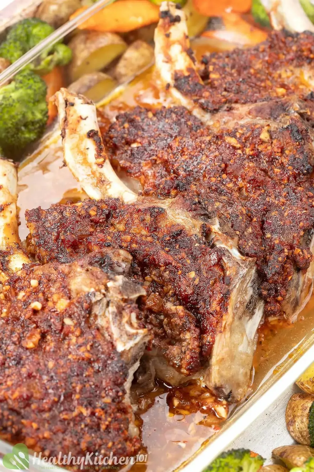 Four golden pork chops and shiny meat juice contained in a glass baking tray, next to some veggies