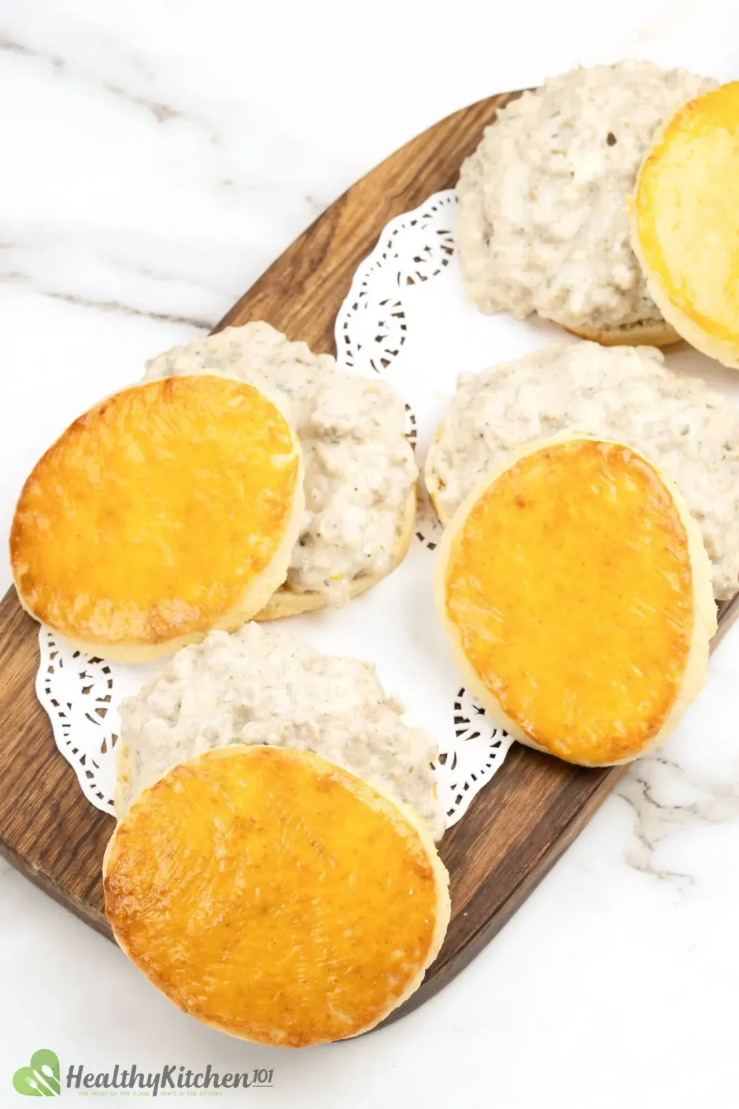 Four pieces of biscuits put over heaps of meaty white gravy, all placed on a wooden cutting board