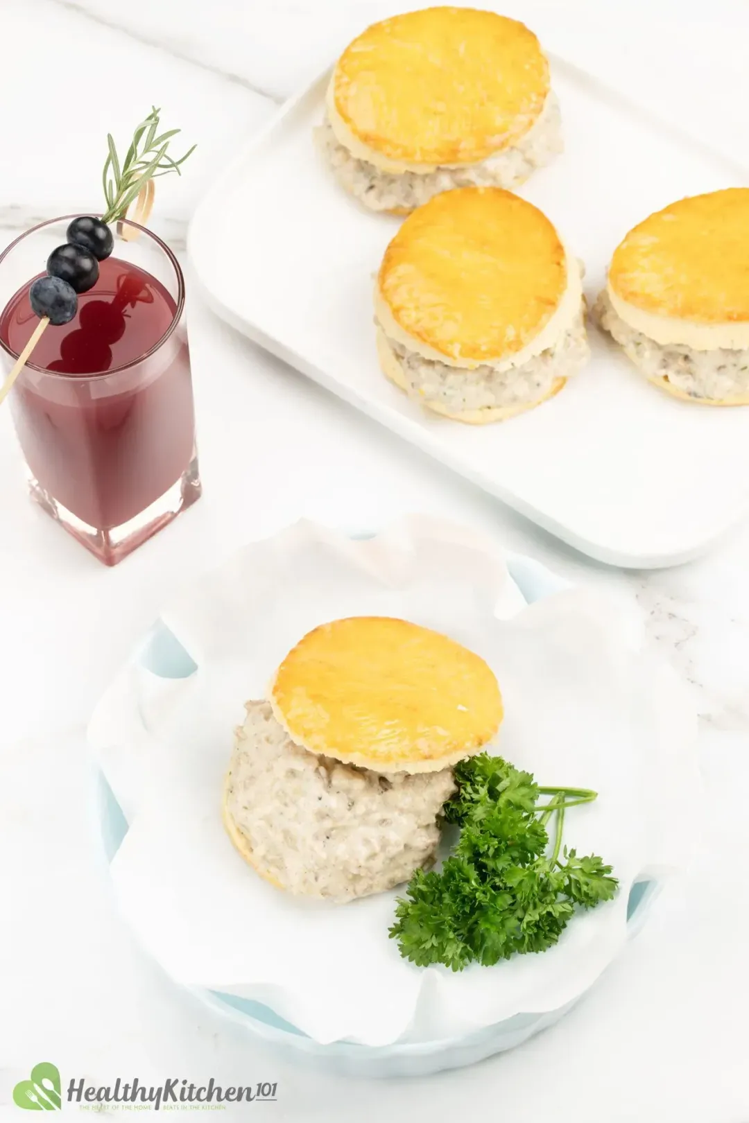 A portion of biscuits and gravy with parsley next to a grape juice and four other portions