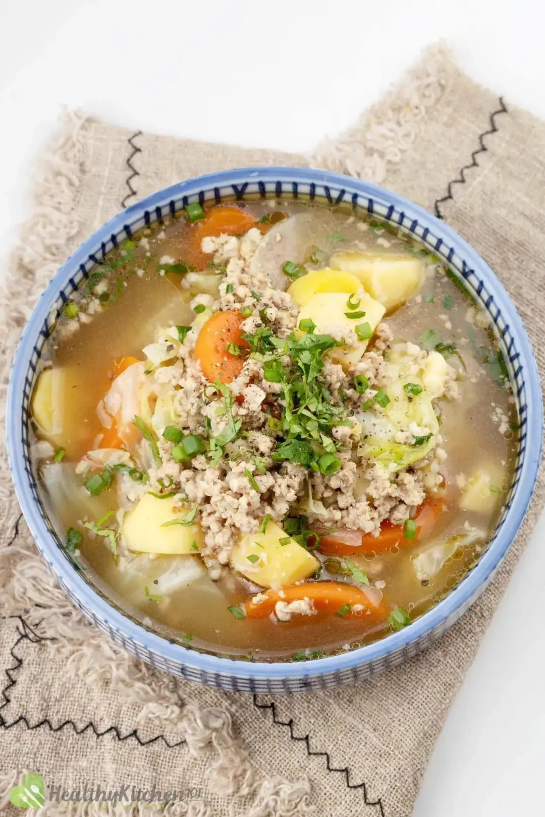 A blue Chinese bowl of cabbage potato carrot soup, topped with lots of chopped green onions
