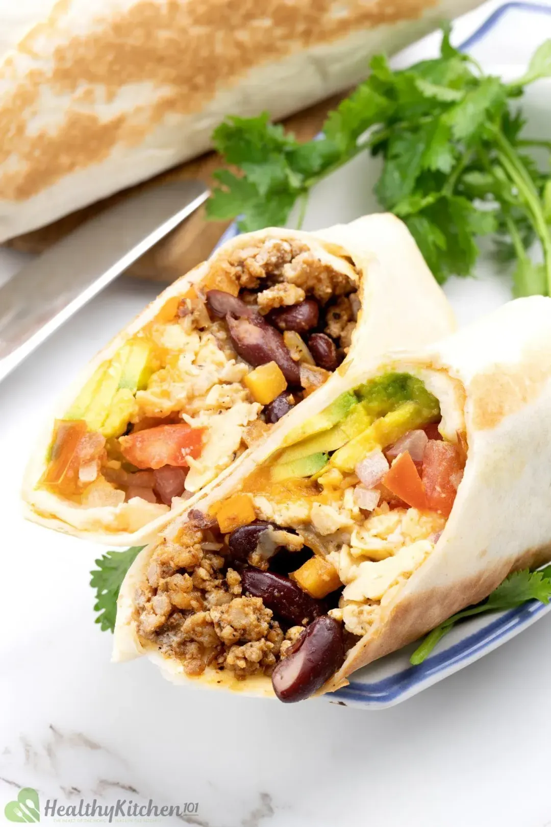 A close-up shot of a burrito roll sliced in half, aligned so that the colorful fillings show, garnished with cilantros