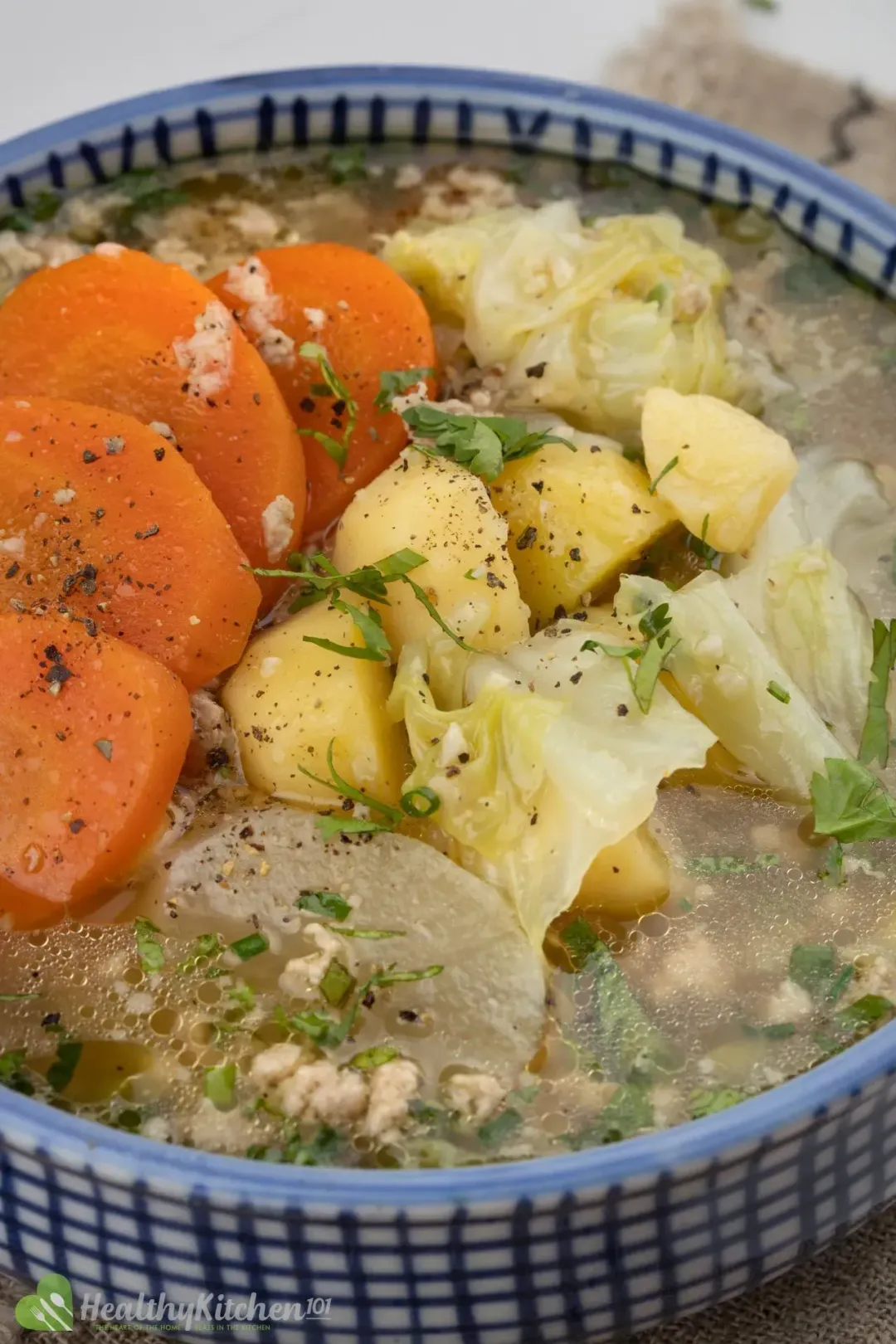 A close up shot of a soup bowl: sliced carrots, cabbage, chunked potatoes, and green onions over the top