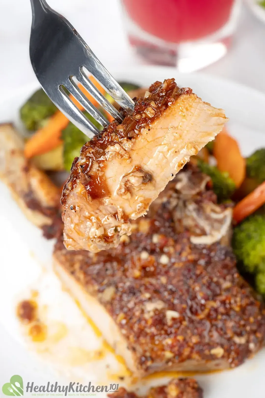 A fork holding a piece of pork cutlet, hovering above a golden pork chop with veggies on the side