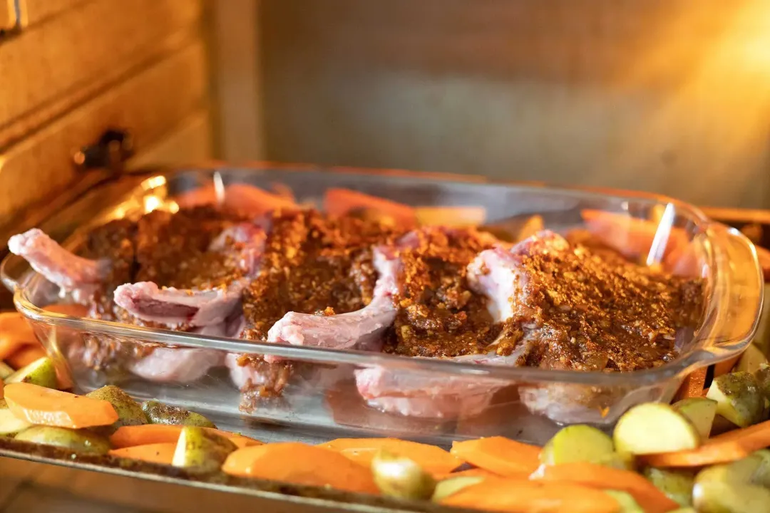 Pork chops covered in sauce in a glass baking tray, surrounded by carrots and broccoli in the oven