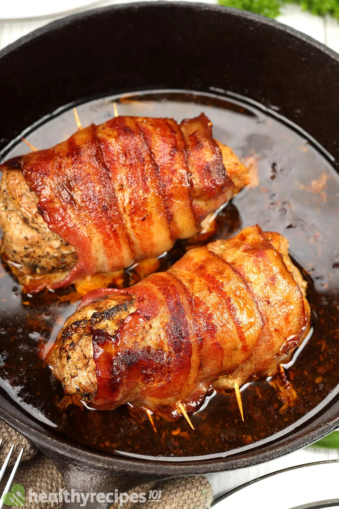 two cooked bacon wrapped pork tenderloin in a cast iron skillet