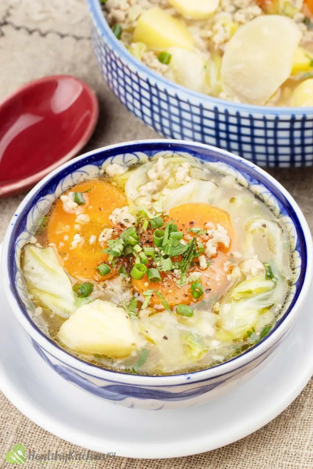 A portion of cabbage potato soup with ground pork, carrots, and green onion in Chinese porcelain bowls