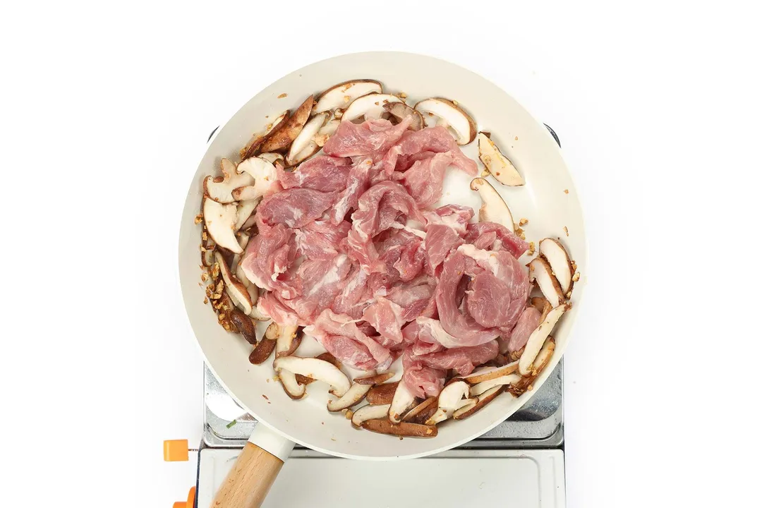 sliced pork with sliced mushroom in a white non-stick skillet