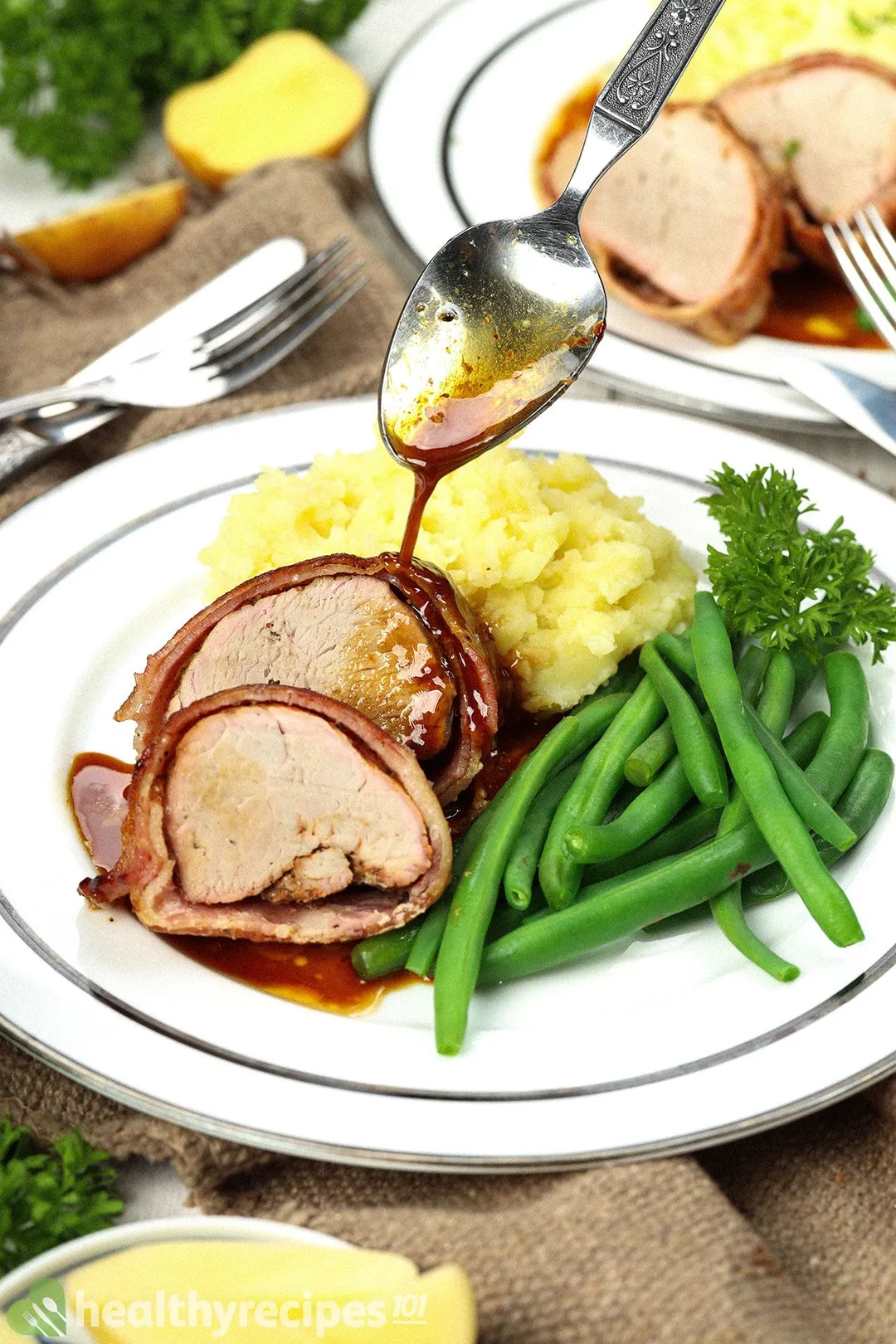 a plate of two slices of cooked pork tenderloin with mashed potato and green beans