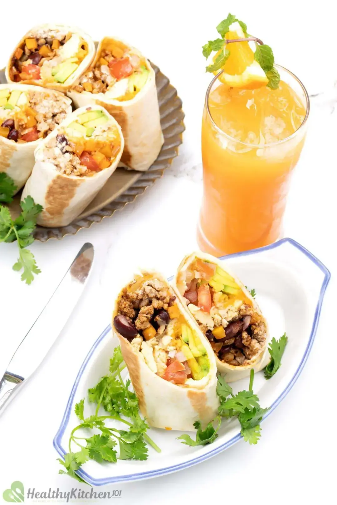 Two plates of burrito rolls cut into segments, showing off colorful fillings, garnished with cilantros and next to a glass of orange juice