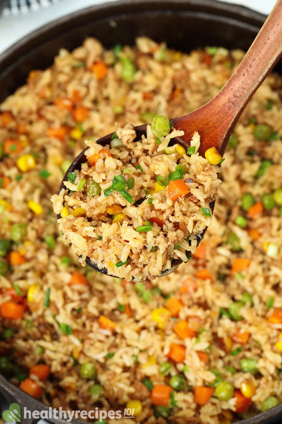 a wooden spoon of fried rice on top of a skillet of cooked rice