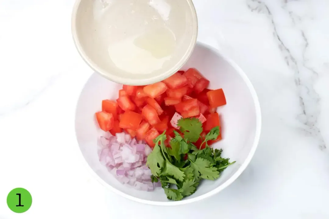 Pouring lemon juice into a bowl of chopped tomatoes, red onions, and cilantros