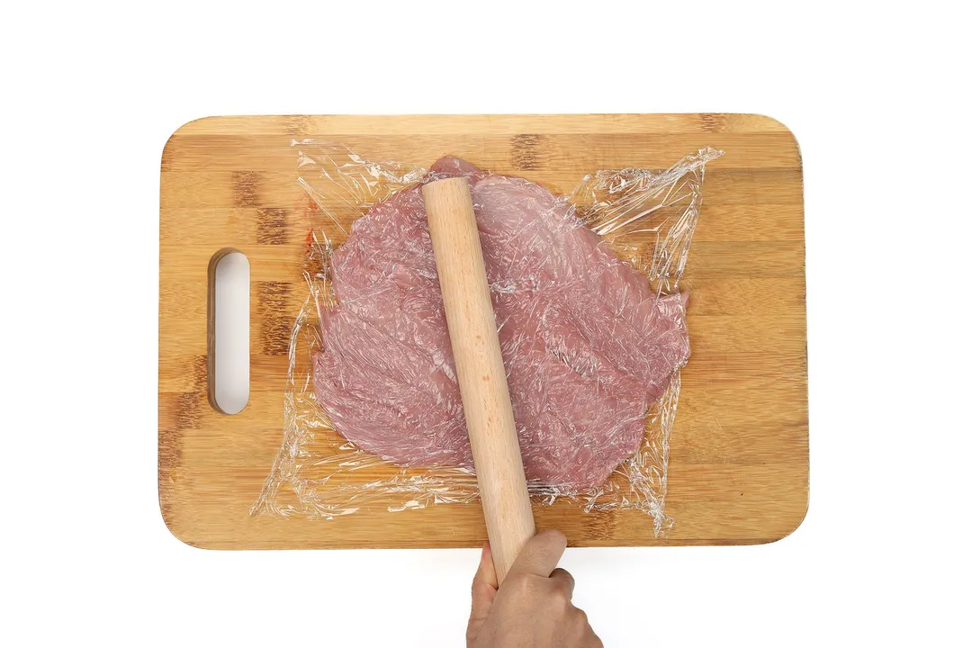 pork loin on cutting board cover with plastic wrap