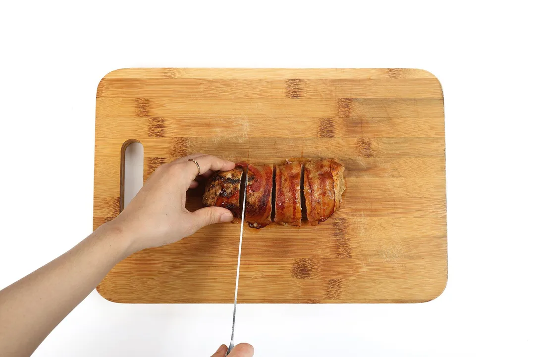 slicing bacon wrapped pork tenderloin on a cutting board by a knife