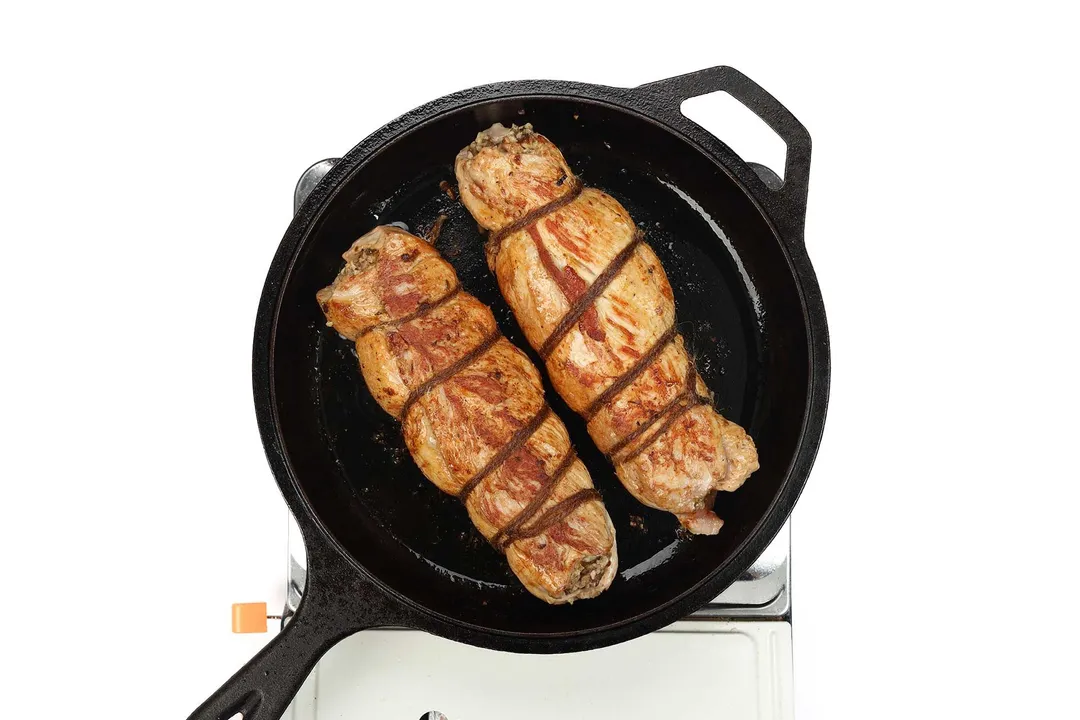 two stuffed pork loin cooking in a cast iron skillet
