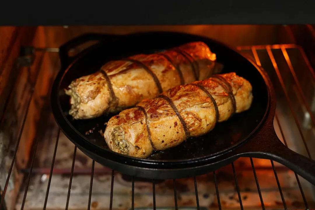 a cast iron skillet with two stuffed pork loin in the oven