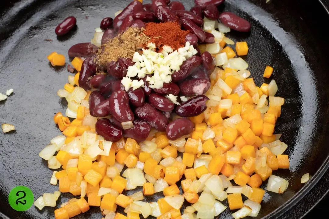 A pile of corn, onion, and kidney beans sauteed in a skillet with paprika, cumin, and chopped garlic on top