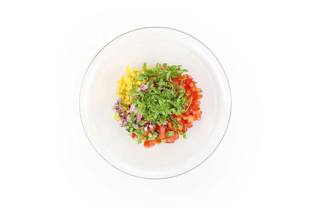 chopped onion, red bell pepper, cucumber, corn and parsley in a glass bowl