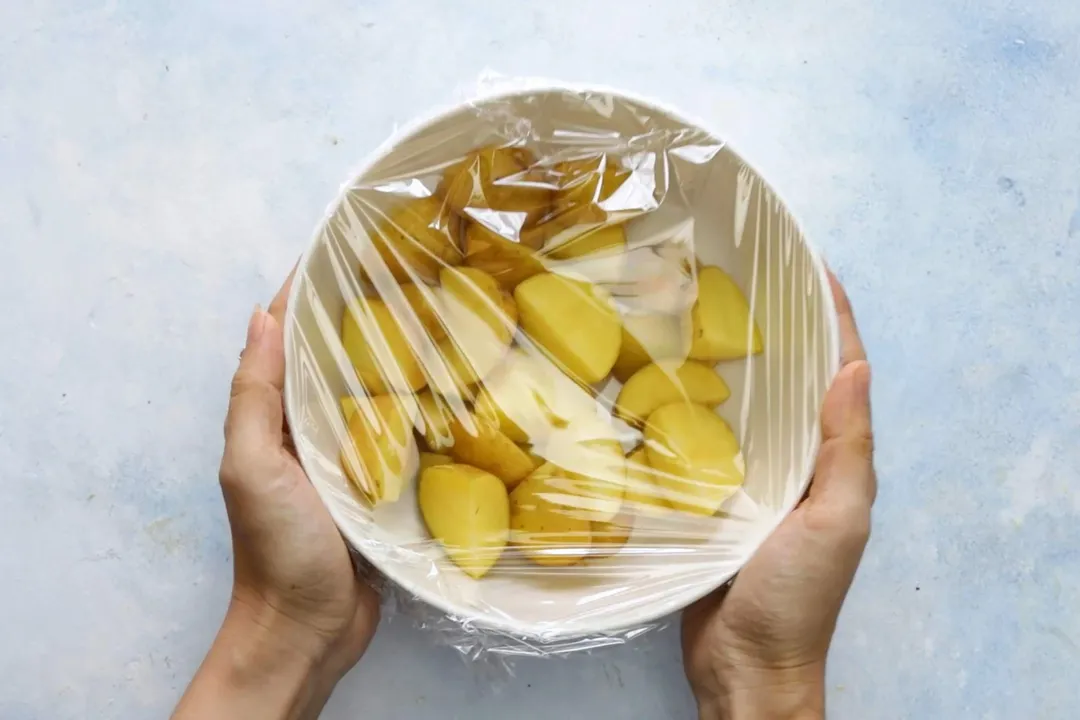 two hands hold a bowl of potato cubes