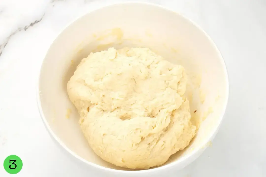 A large piece of dough resting in a while bowl