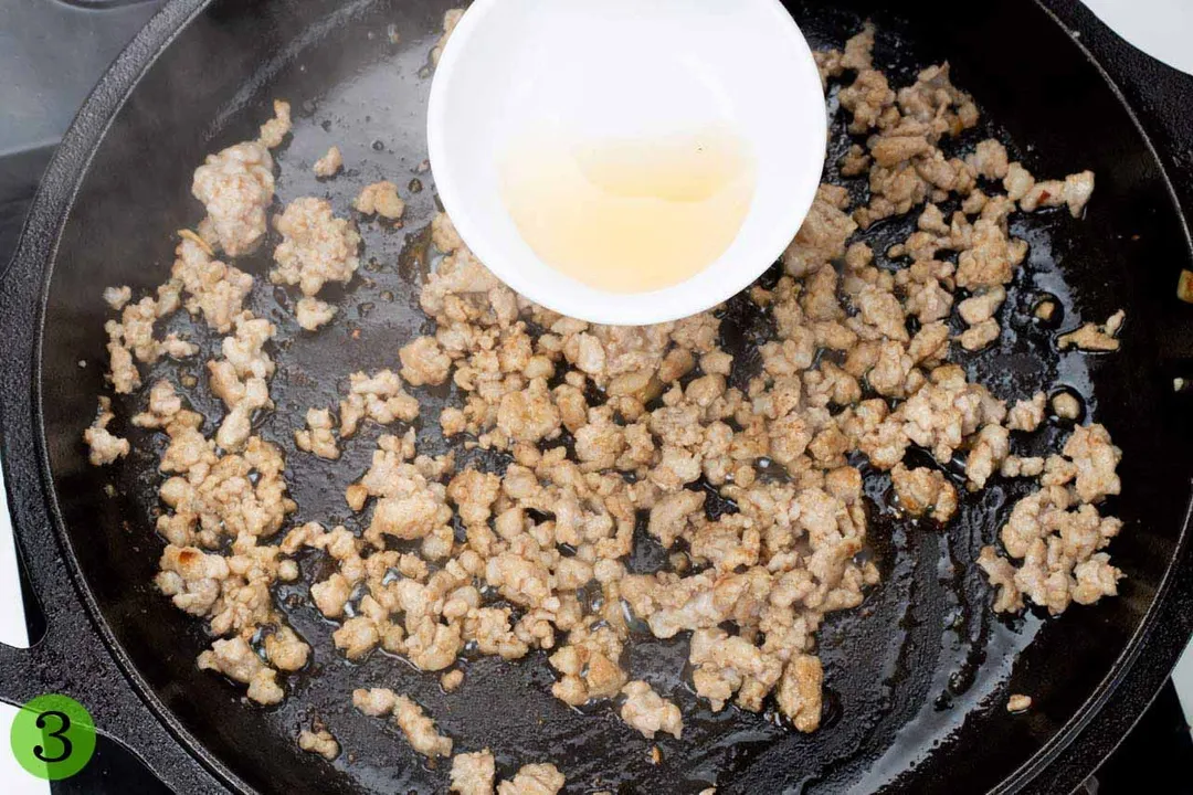 Wine poured on top of some ground pork sauteed in a skillet