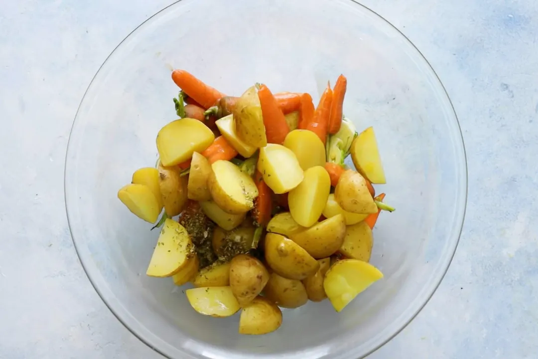a glass bowl of potato cubes, carrot and seasoning