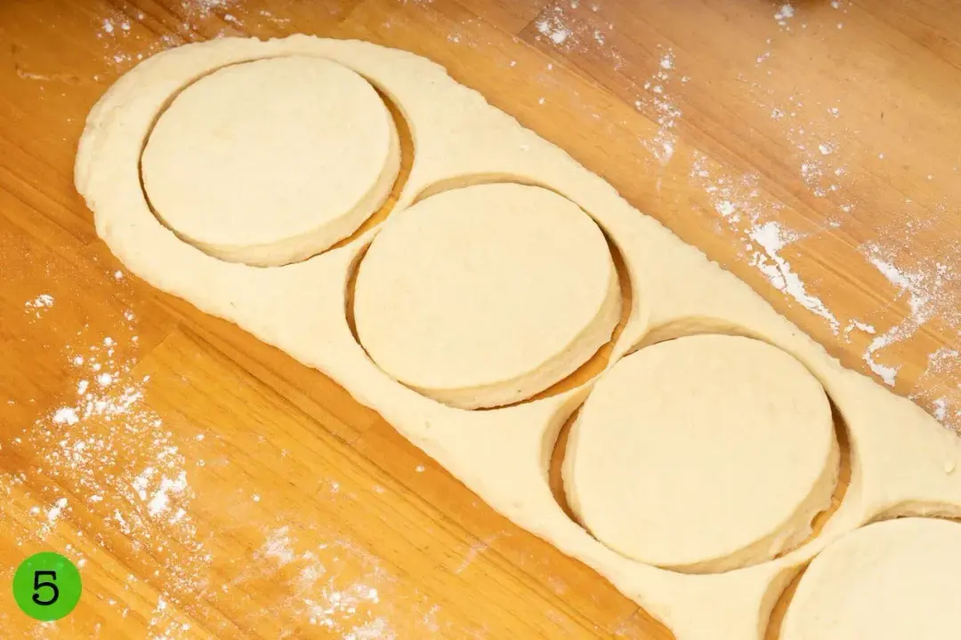 A thick sheet of dough on a wooden working surface, cut into four circles