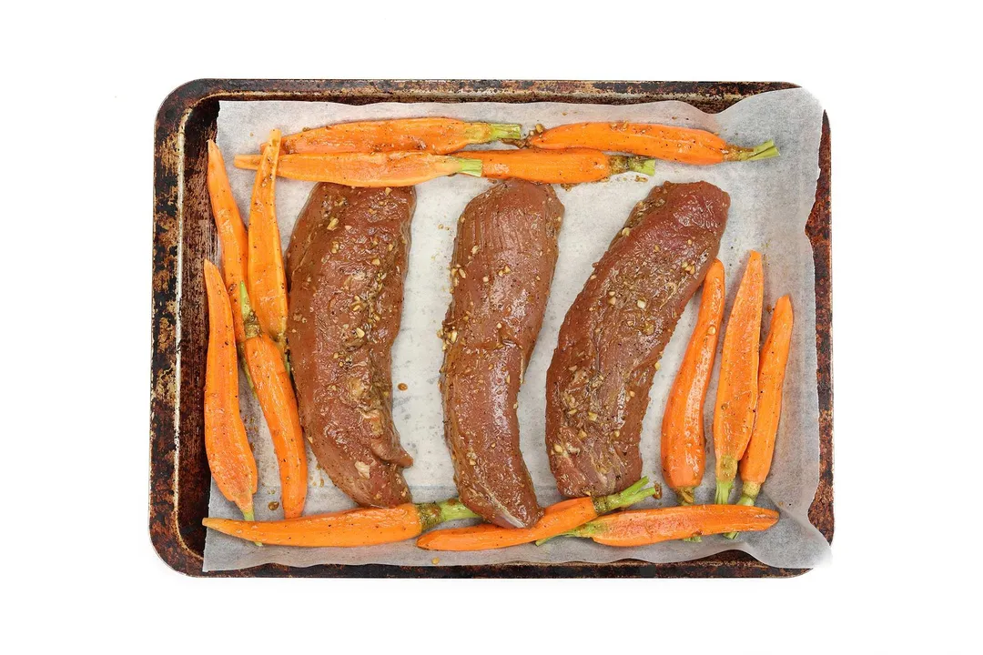 three marinated pork tenderloin and slices carrot on a baking tray