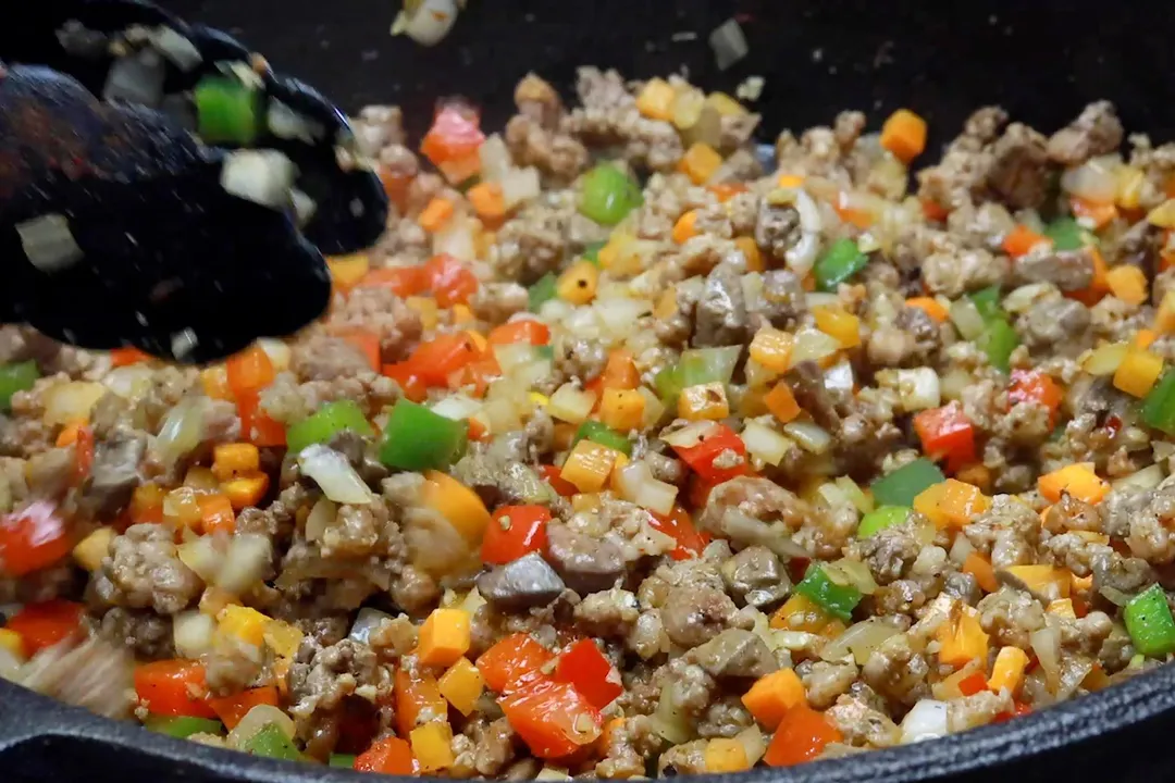 cooking chicken liver and vegetables in a skillet