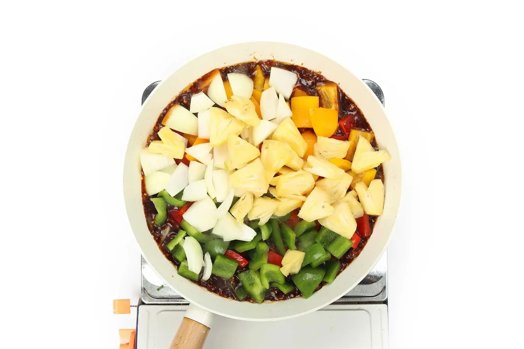 chopped bell pepper, pineapple and sauce cooking in a skillet