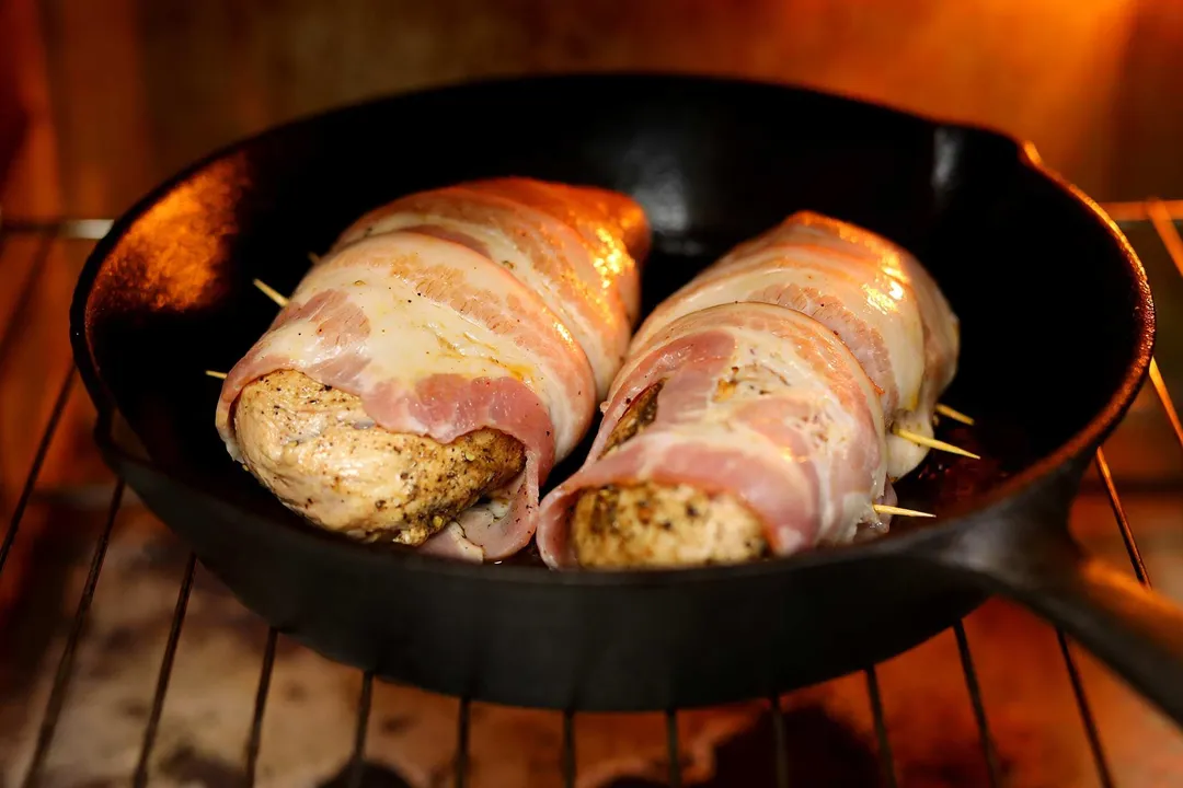 a cast iron skillet of two bacon wrapped pork tenderloin in the oven