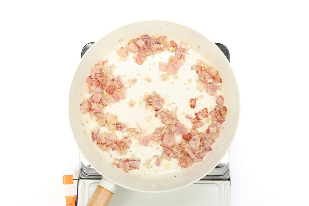 minced shallot garlic and onion with bacon cooking in a skillet