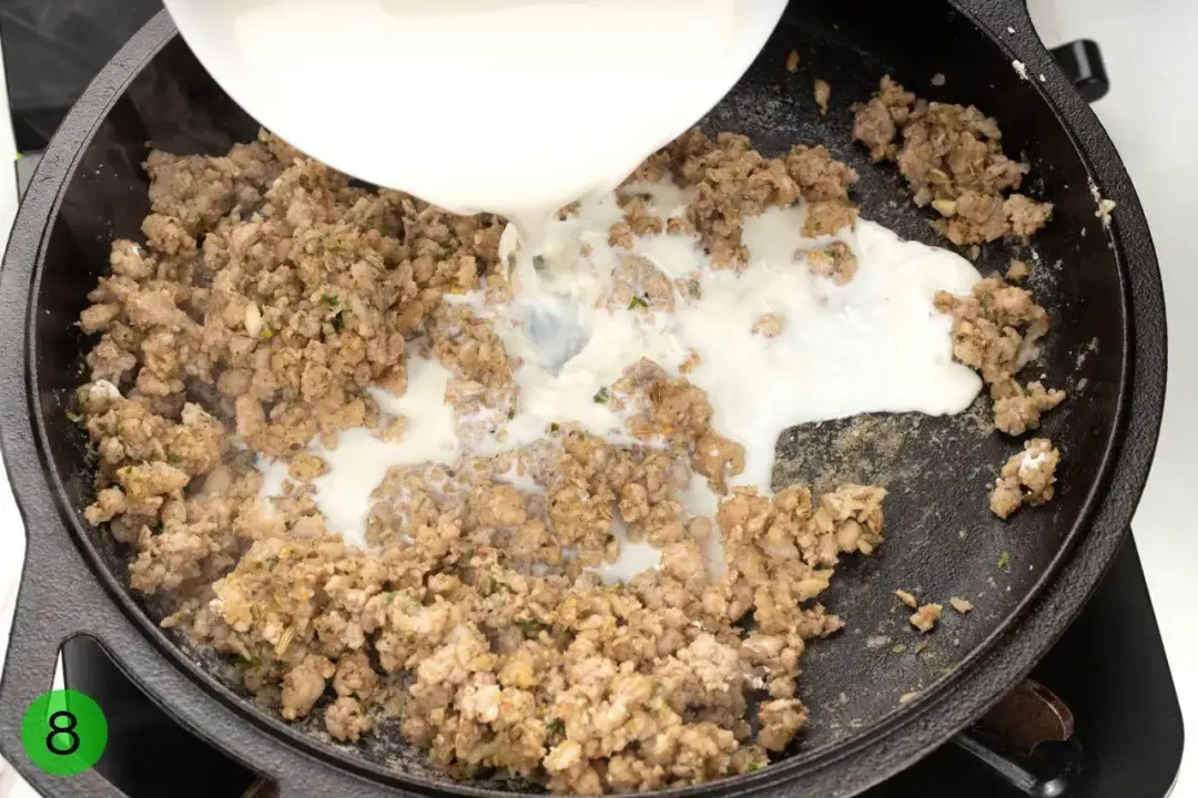 A white liquid poured into cooked ground meat in a black cast iron skillet