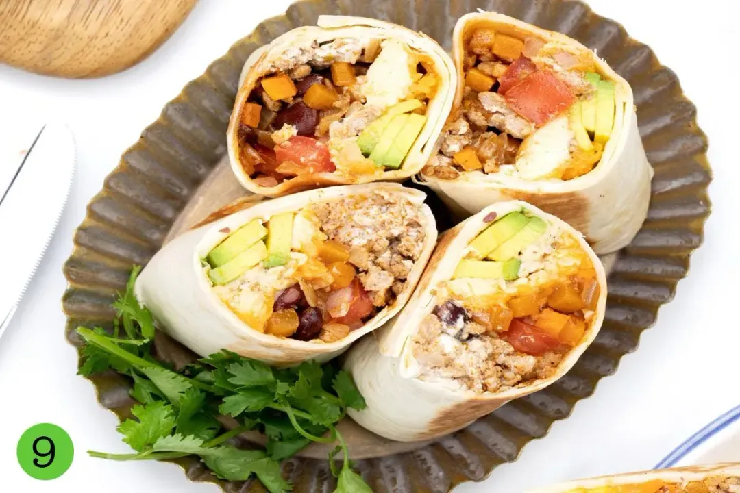 A plate of four rolls of burritos cut up, showing colorful fillings